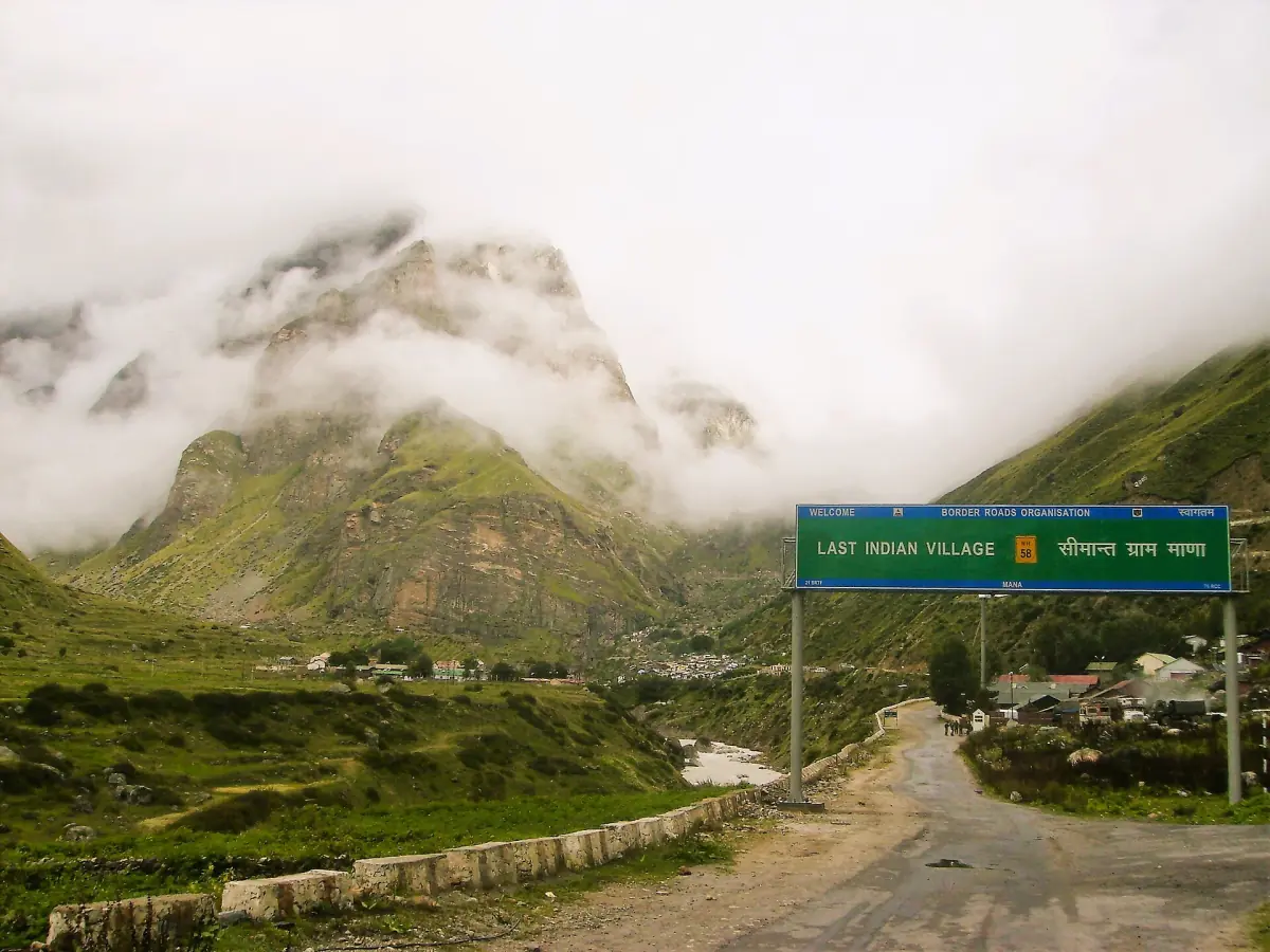 Mana village in a green valley with a road and low cloud on the mountains