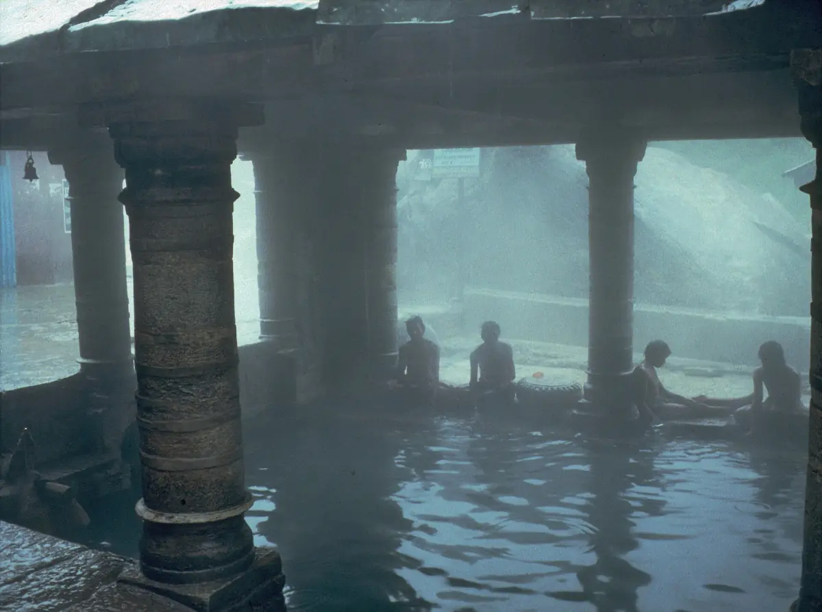 Covered hot spring pool with stone pillars and steam near the Alaknanda
