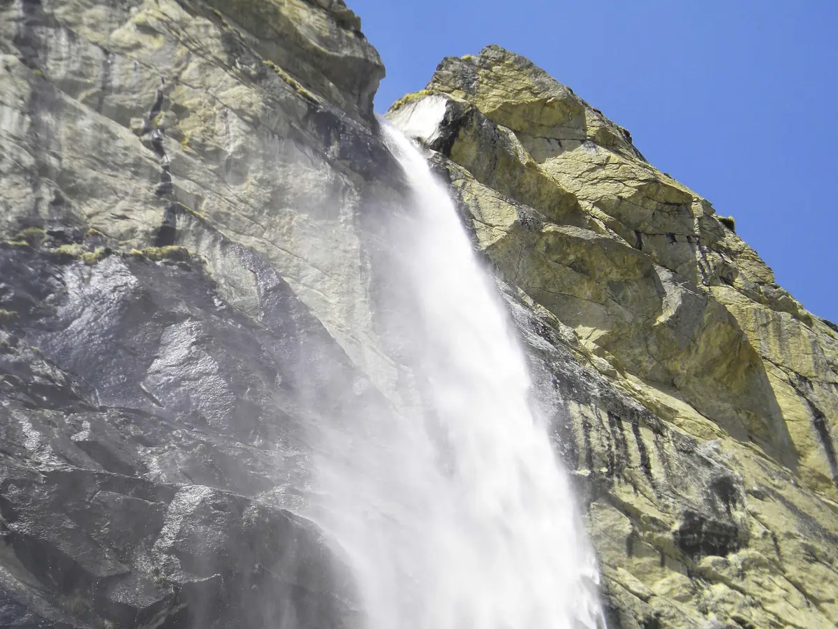 Vasudhara Falls dropping down a steep rock cliff under blue sky