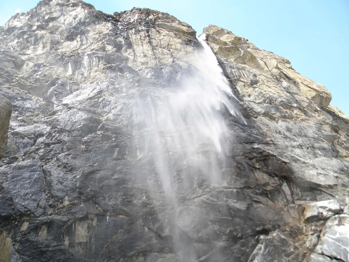 Spray of Vasudhara Falls drifting down a grey rock face